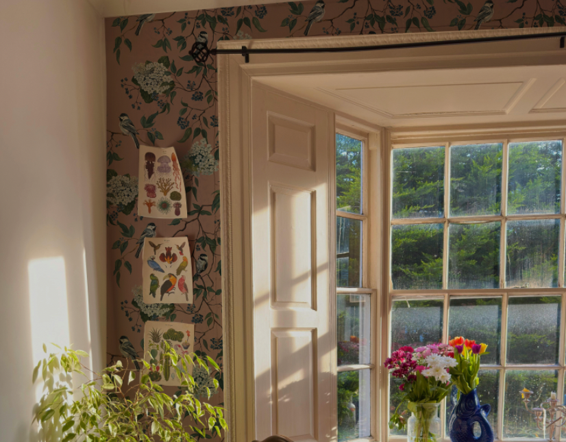 Room with floral wallpaper, a window, and a vase of flowers.