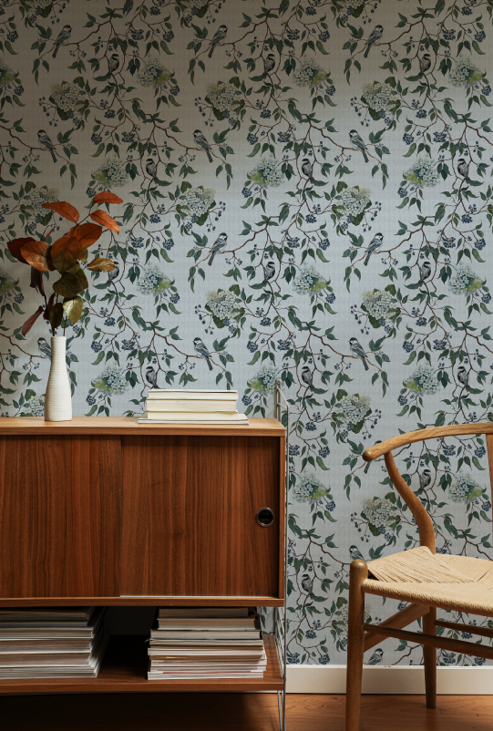 Room interior with wooden furniture against a floral wallpapered wall.
