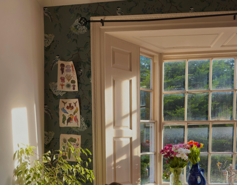 Room with floral wallpaper, open door leading to a garden, and decorative items on the wall.