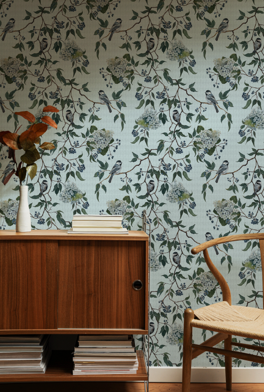 Room interior with wooden cabinet, vase with flowers, and chair against floral wallpaper.