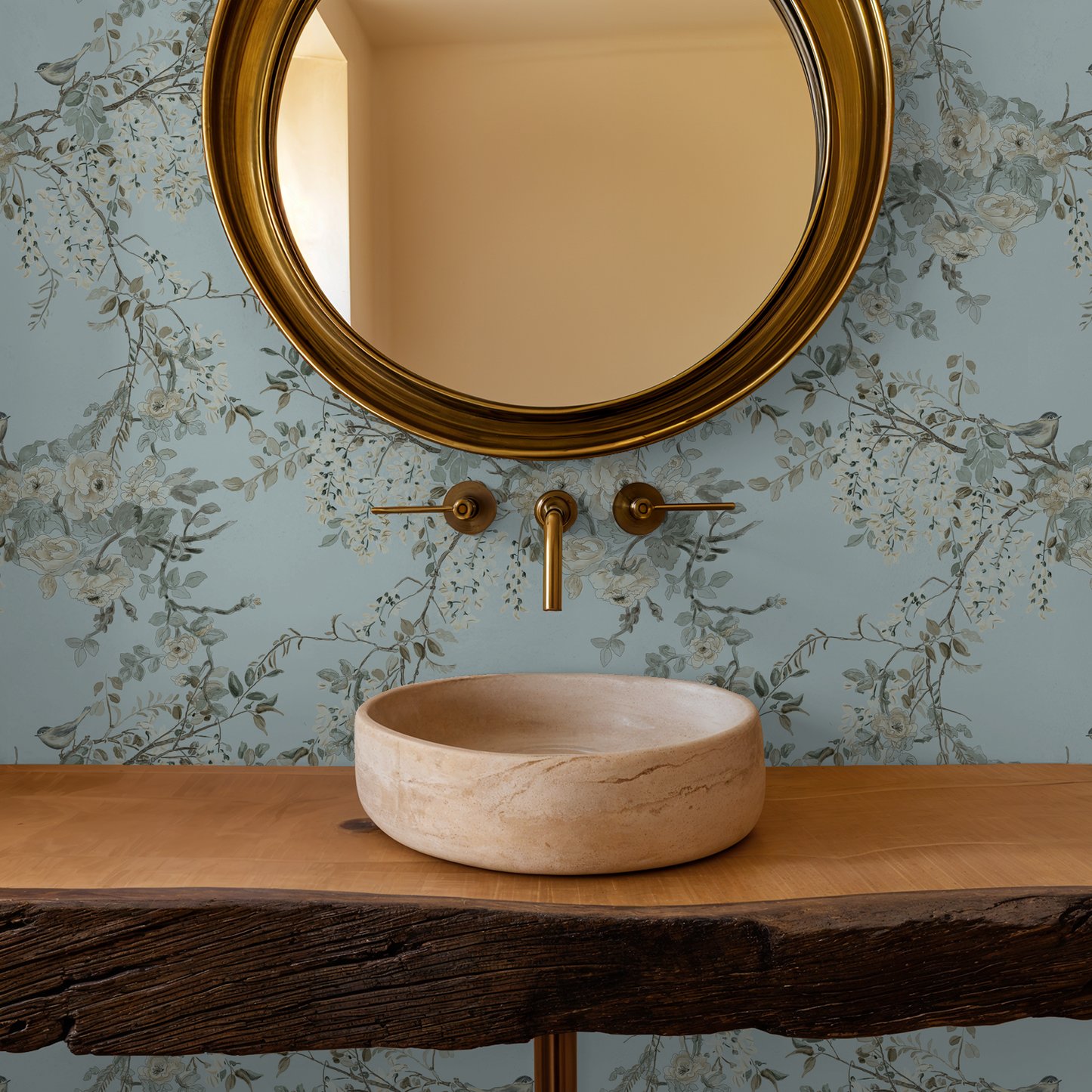 Bathroom vanity with a round beige sink, gold faucet, and mirror against floral wallpaper.
