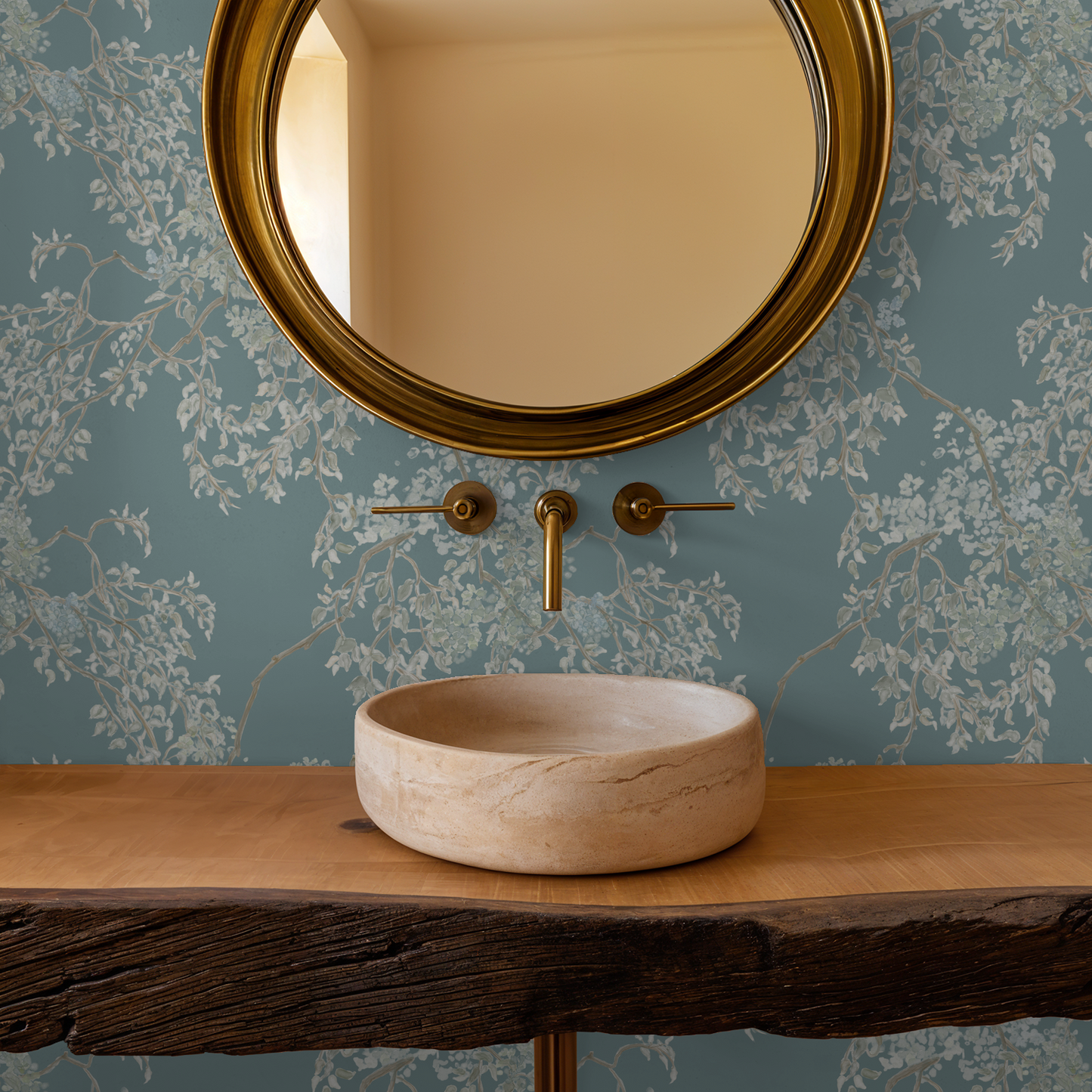 Bathroom setup with a round mirror, faucet, and stone sink against a floral wallpapered wall.