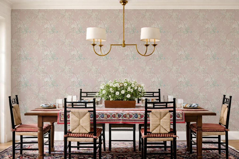 Dining room with wooden table and chairs against a floral wallpapered wall.