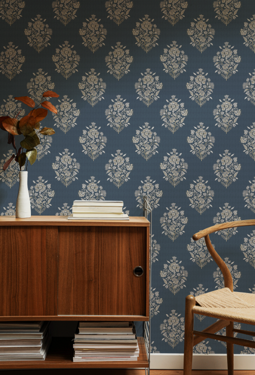 Room interior with wooden cabinet, chair, and floral arrangement against a patterned blue wall.