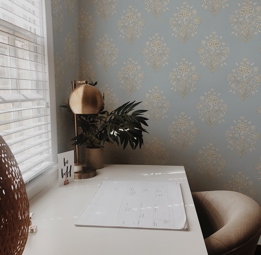 Home office with a desk, plant, and decorative items against a patterned wall.