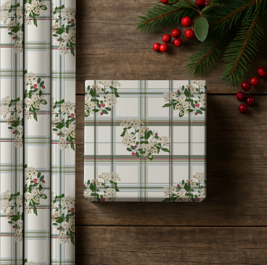 gift box wrapped with a floral and plaid design on a wooden surface with holly berries and branches.