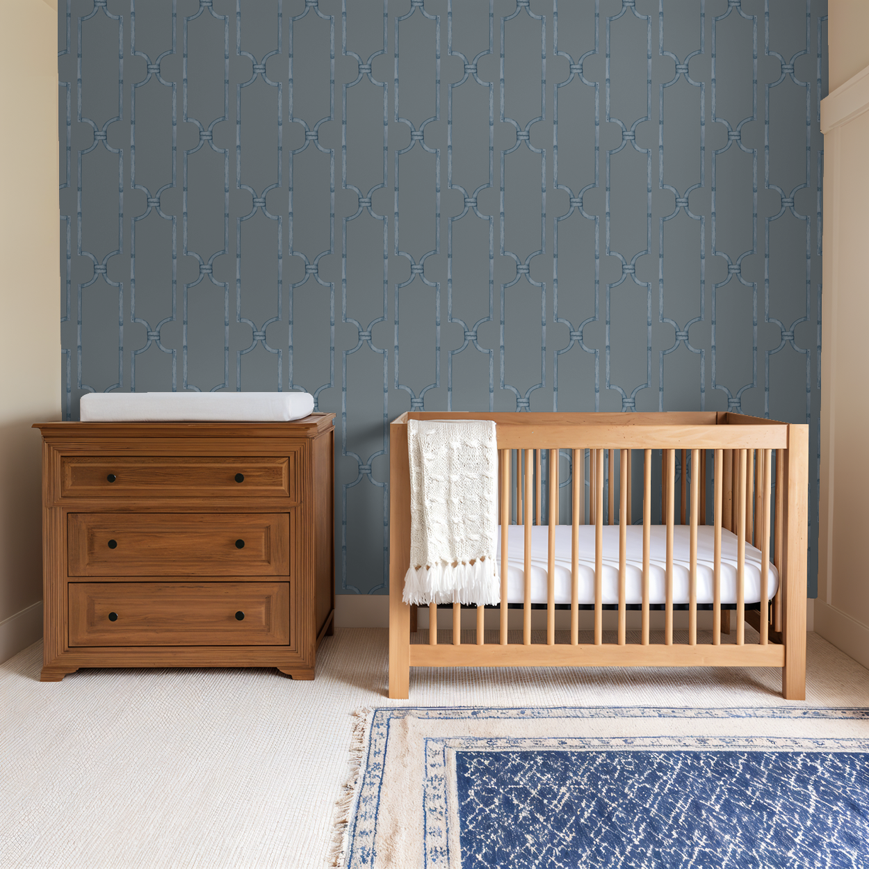 Blue geometric trellis wallpaper in nursery with wooden crib and dresser.