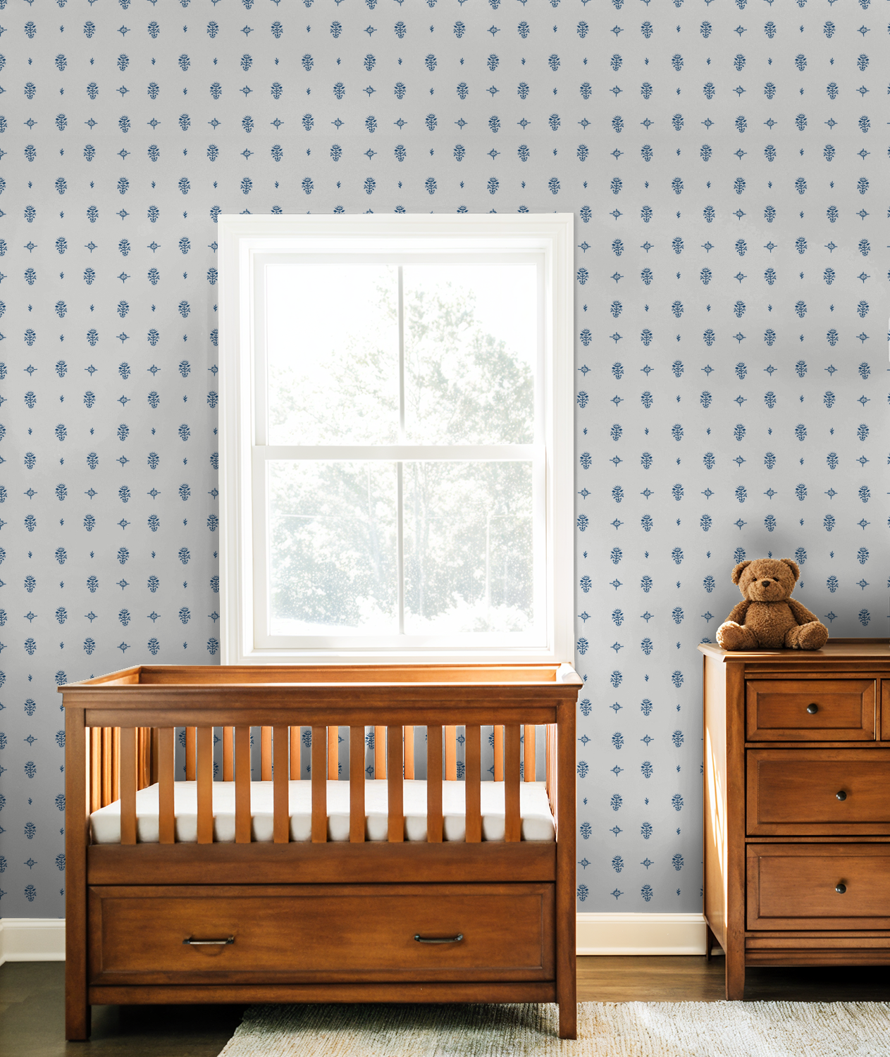 Cream and blue botanical wallpaper in a nursery with wooden crib and dresser.