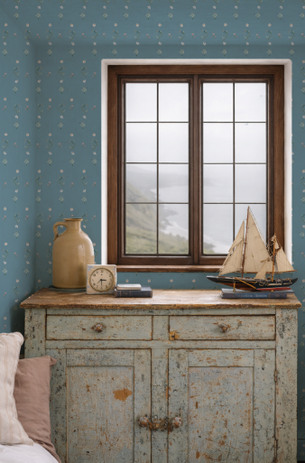 Vintage-style room with wooden cabinet, window, and decorative items against a blue wallpaper.