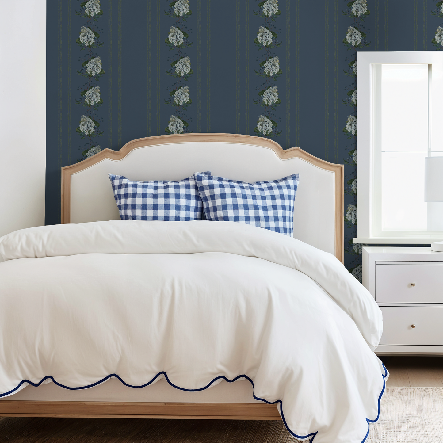 Bedroom with deep blue floral hydrangea stripe wallpaper, white bed, and checkered pillows.
