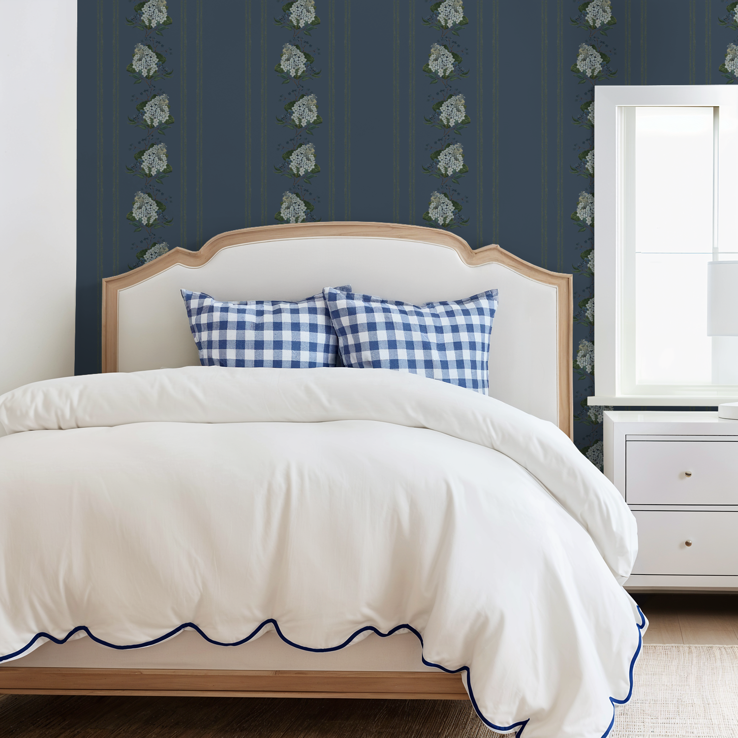 Bedroom with deep blue floral hydrangea stripe wallpaper, white bed, and checkered pillows.