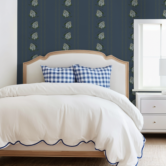 Bedroom with deep blue floral hydrangea stripe wallpaper, white bed, and checkered pillows.