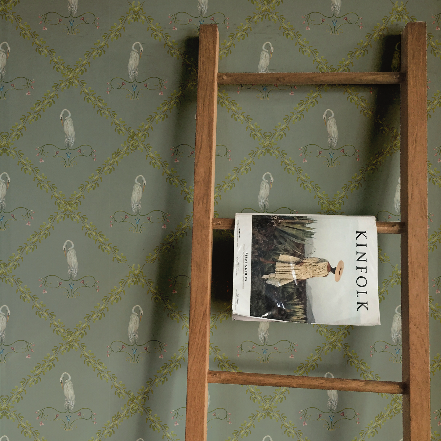 Wooden ladder against a wall with decorative wallpaper featuring birds and geometric patterns.