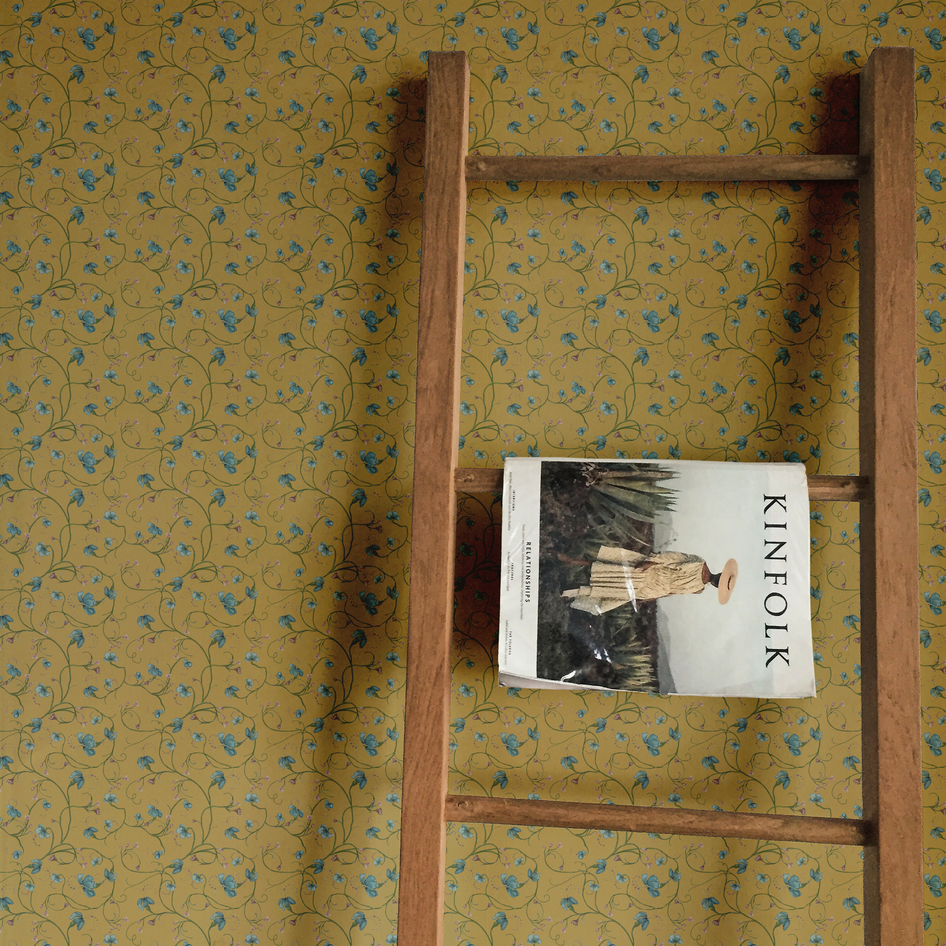 Wooden ladder against a yellow floral-patterned wall with a book titled 'KINFOLK' on one of its rungs.
