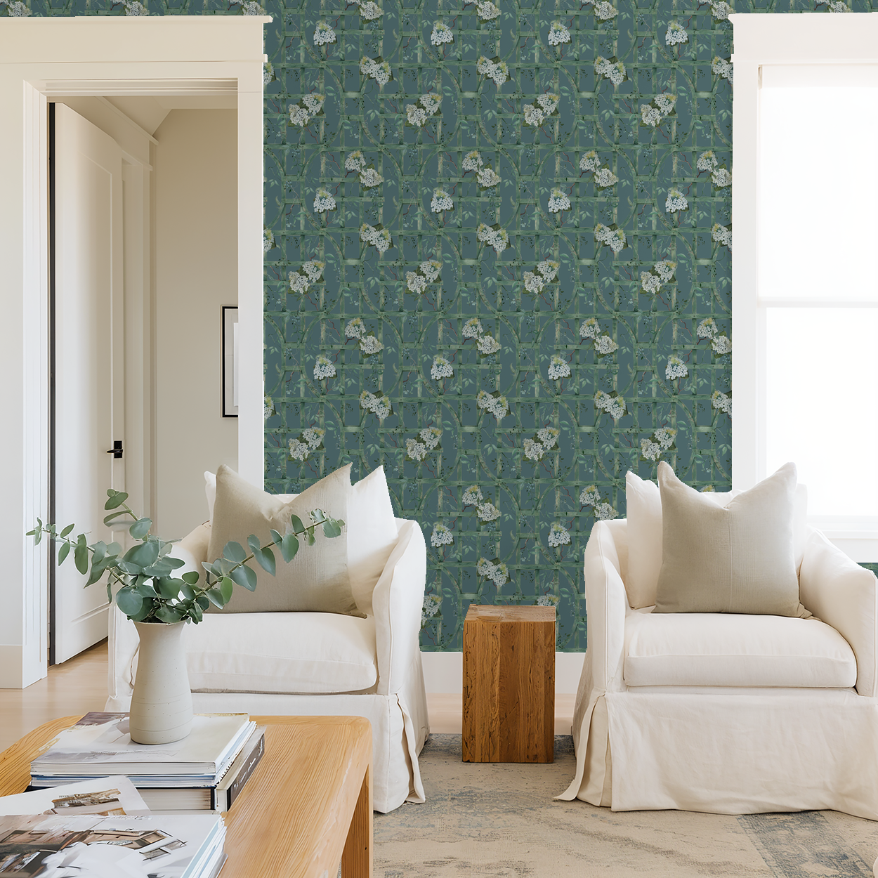 Living room with green trellis and white hydrangea wallpaper, white chairs, wooden table.