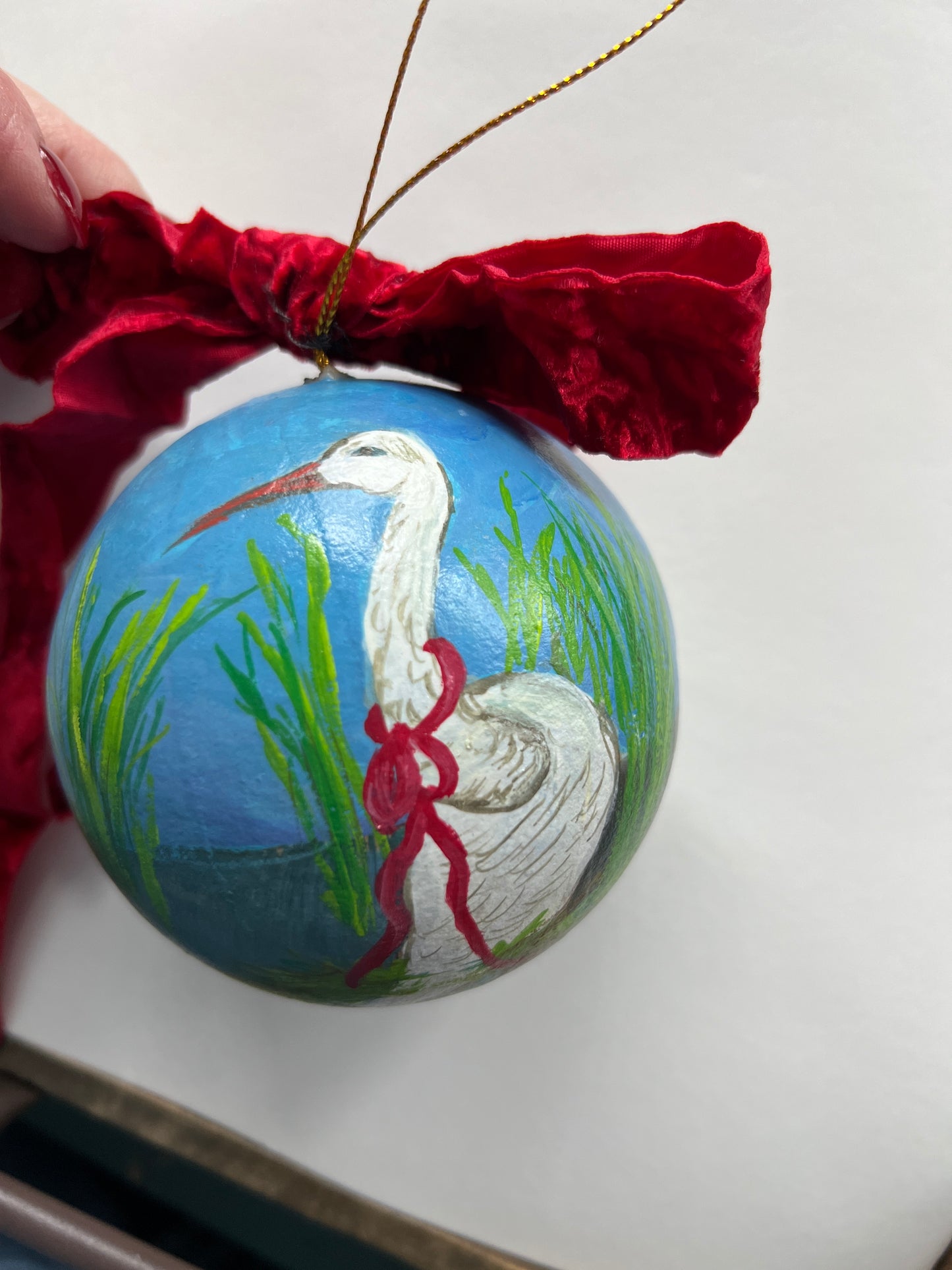 Decorative ornament with a stork and baby design on a blue background, tied with red ribbon.