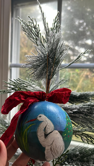 Decorative Christmas ornament with a bird design held in front of a window with a view of trees.