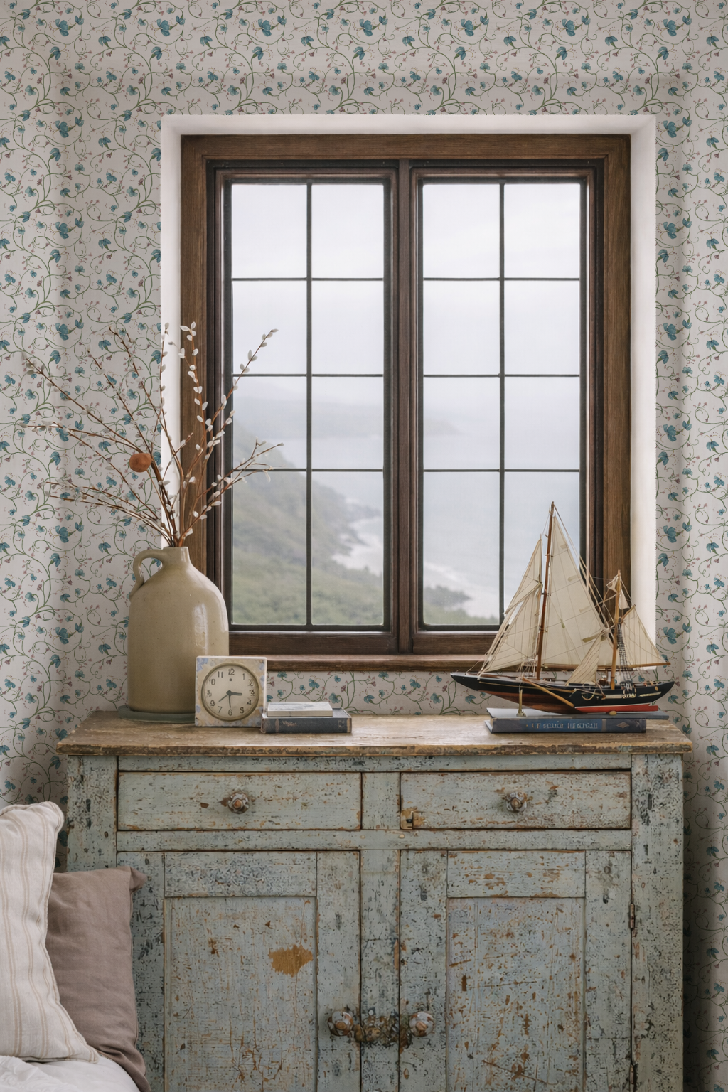 Vintage-style cabinet with a clock, vase, and model sailboat against a floral wallpapered wall.