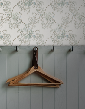 Wooden hanger on a hook against a floral wallpapered wall.