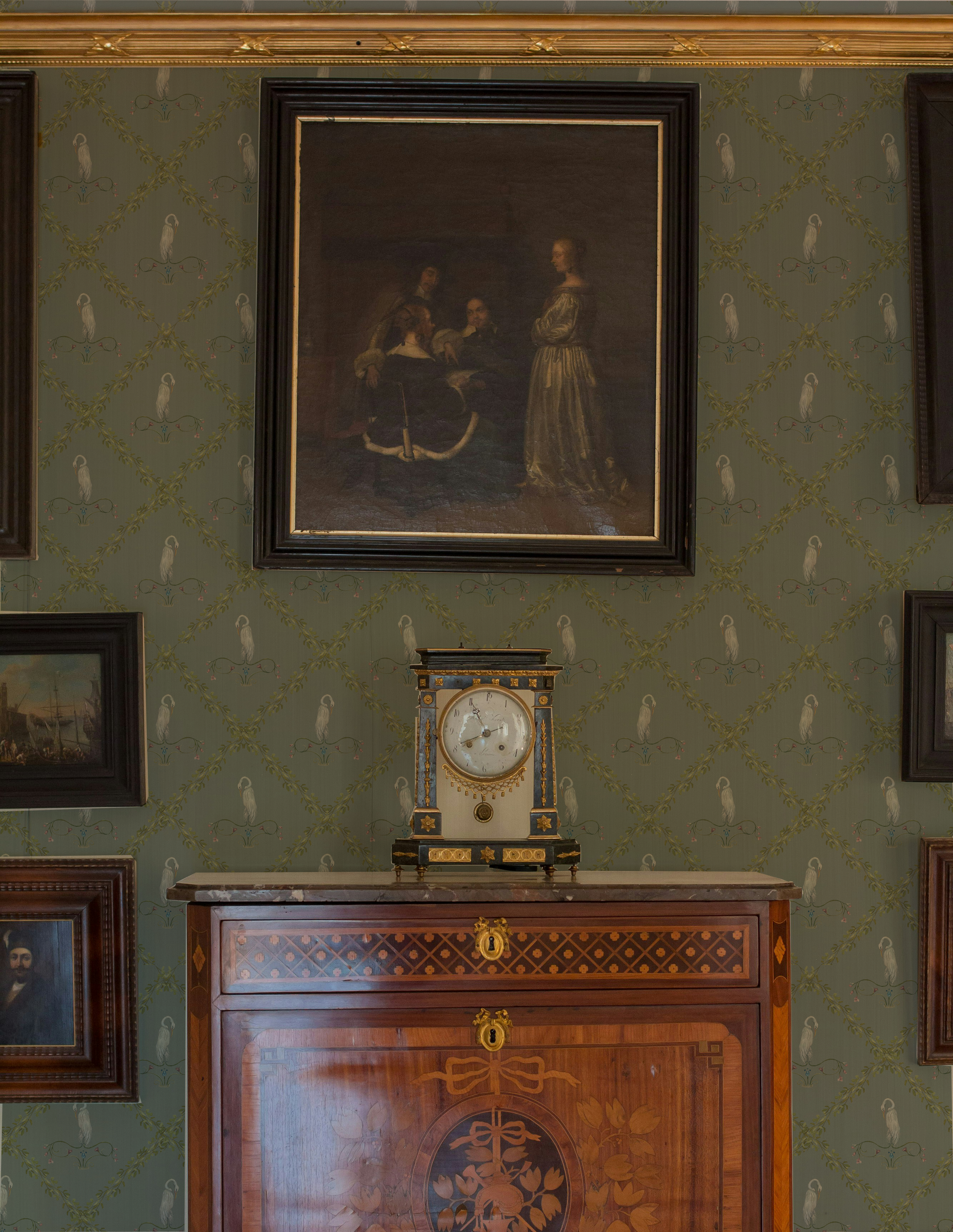 Decorative wall with framed portraits and a clock on a wooden cabinet.