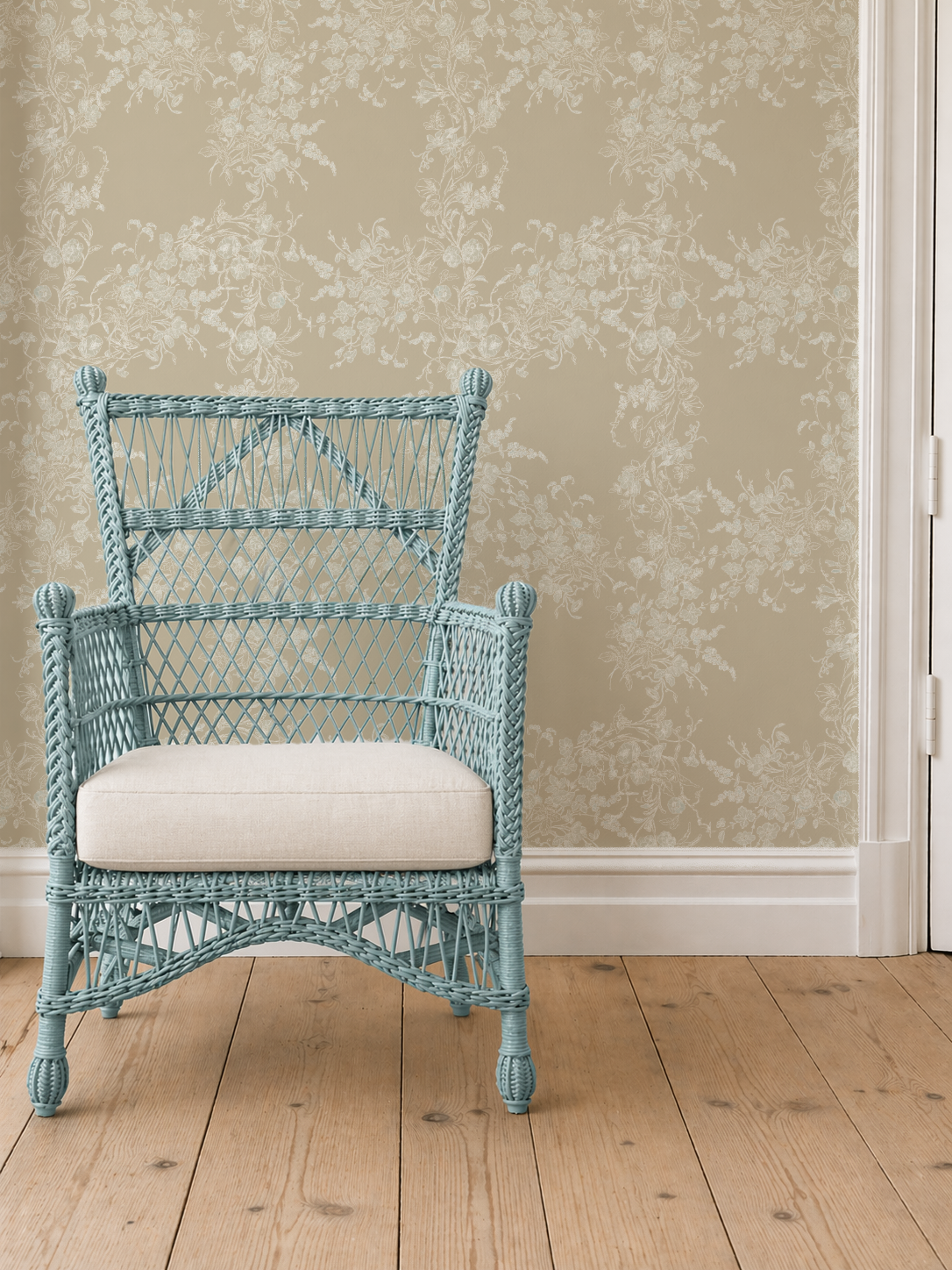 Blue wicker armchair with a white cushion against a floral wallpapered wall.