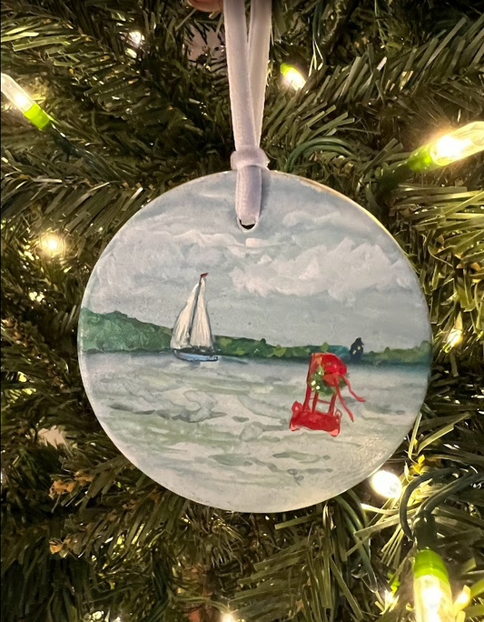 Decorative Christmas ornament with a sailboat and red chair on a tree.