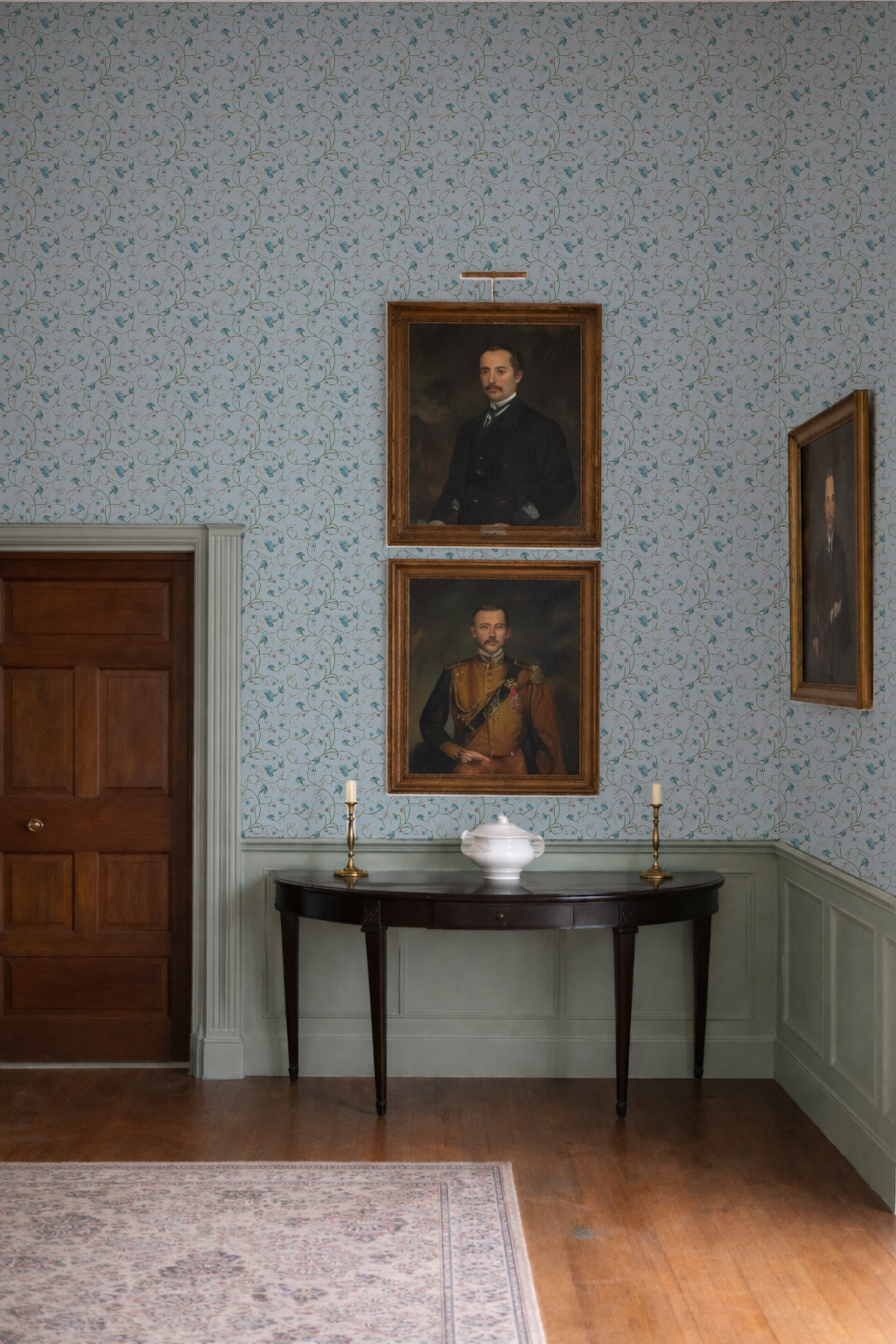 Room with portraits on the wall and a table with a vase and candles.