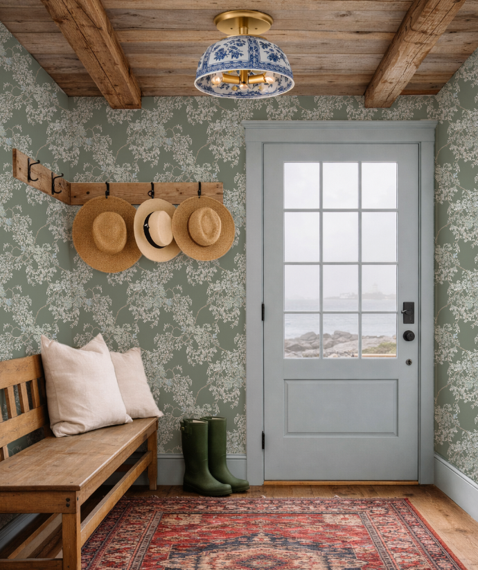 Foyer with floral wallpaper, wooden bench, hats on a hook, and a door with a view.