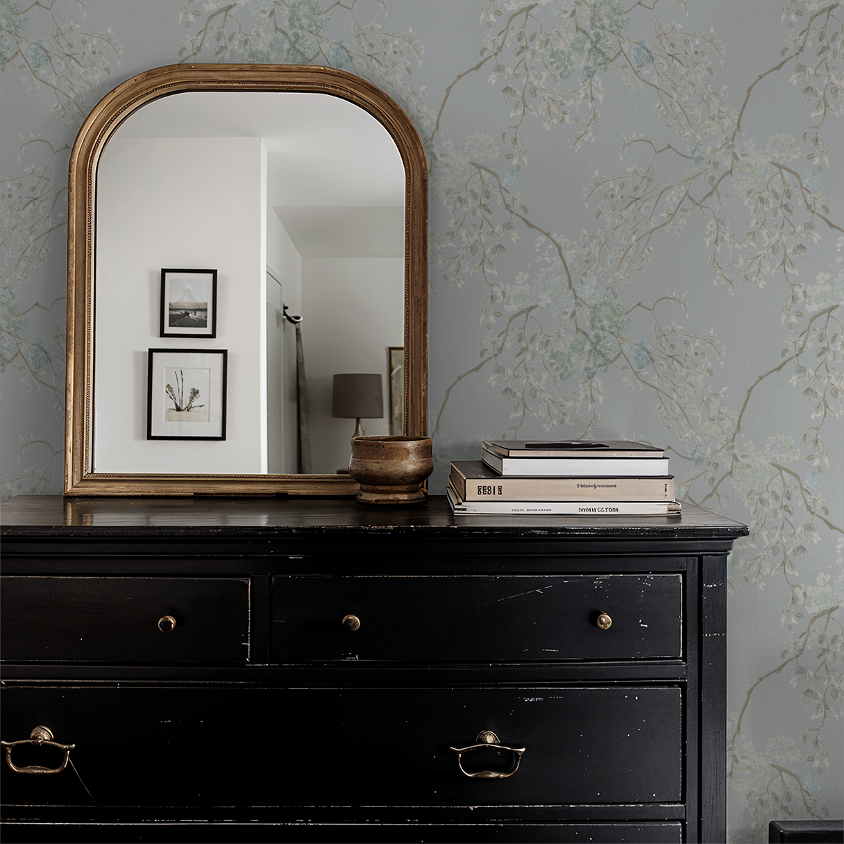 Black dresser with gold-framed mirror and decorative items against a floral wallpapered wall.