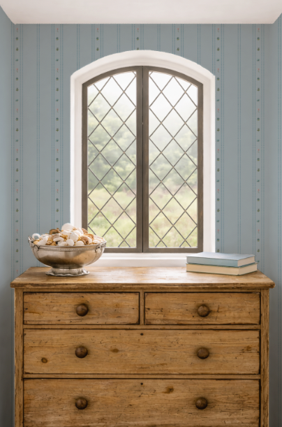 Wooden dresser with a bowl of seashells and books against a striped wall.